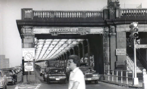 Photo of 4 motor vehicle lanes of a bridge reaching the ground.
A beautiful stone facade and promenade are at the bridge terminus.
In the center of the facade are stairs leading to the promenade.